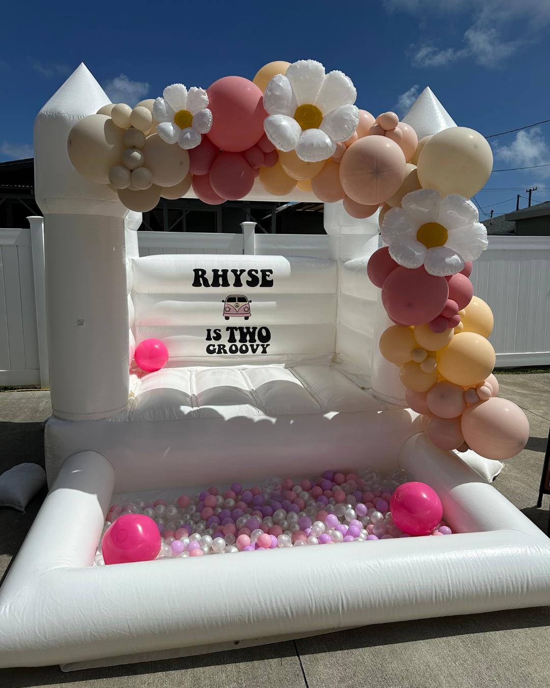 A white bouncy castle with balloons and flowers on it.
