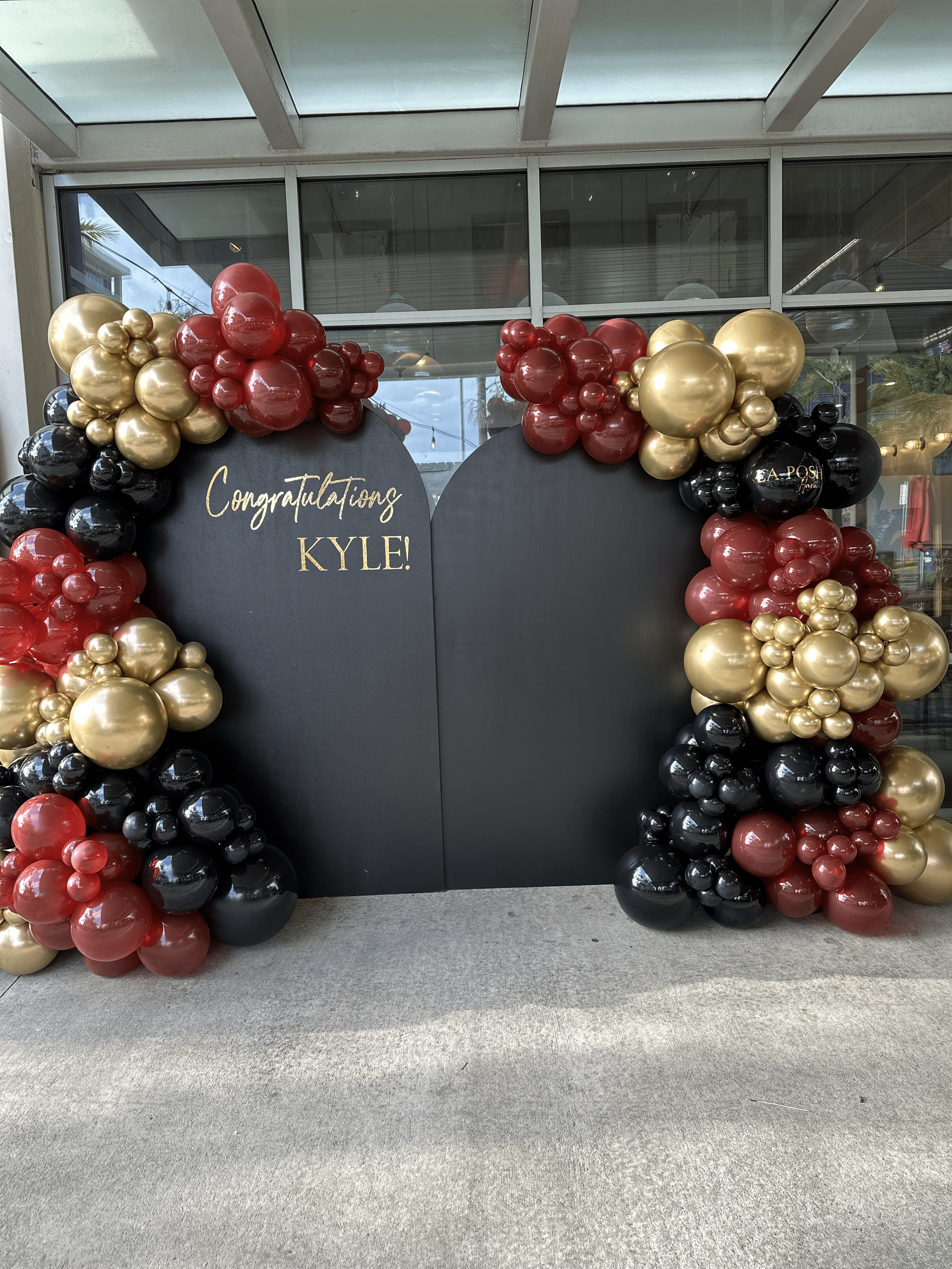 A wall covered in red , black and gold balloons.