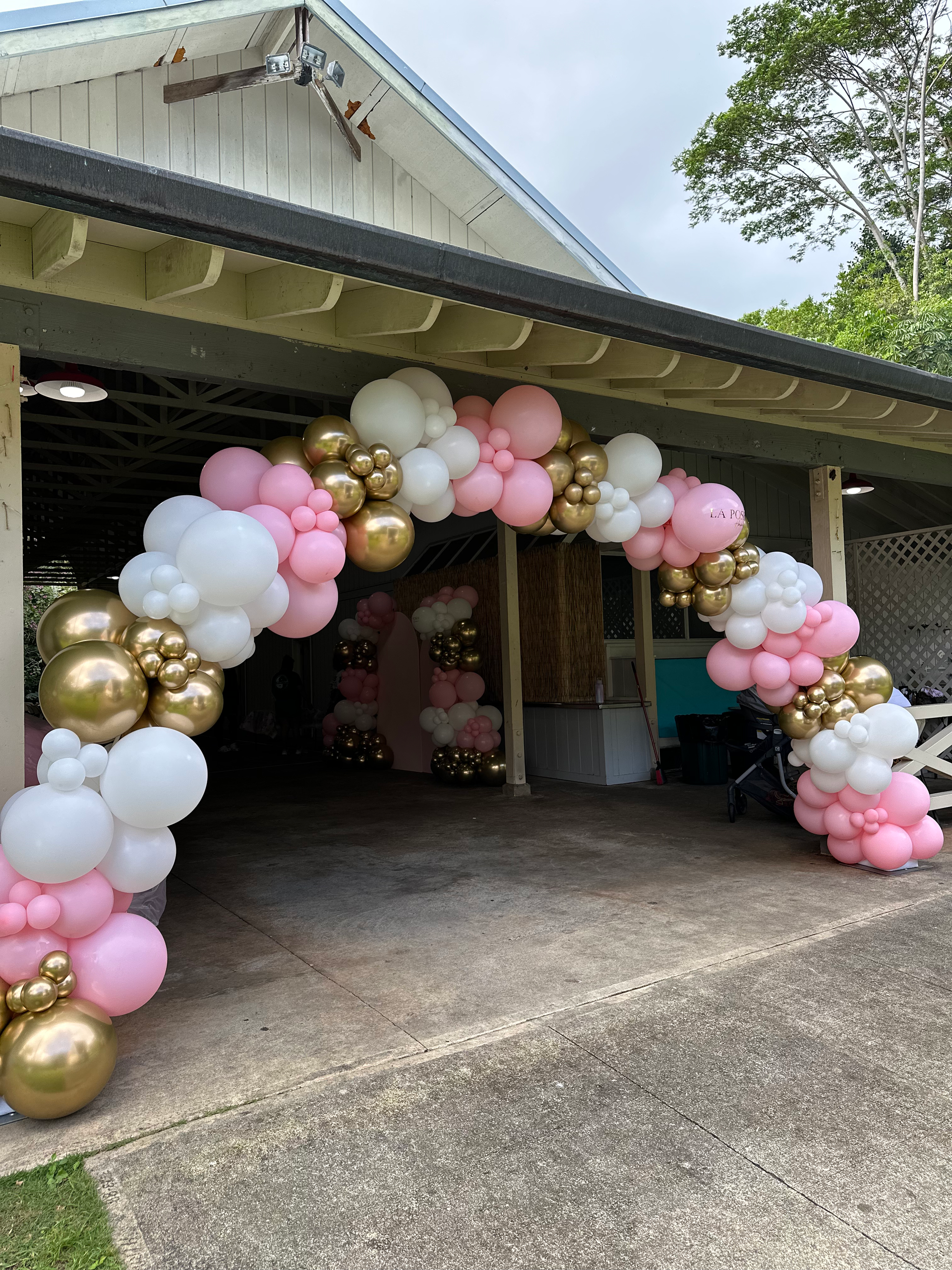 A bunch of pink , white and gold balloons are sitting in front of a house.