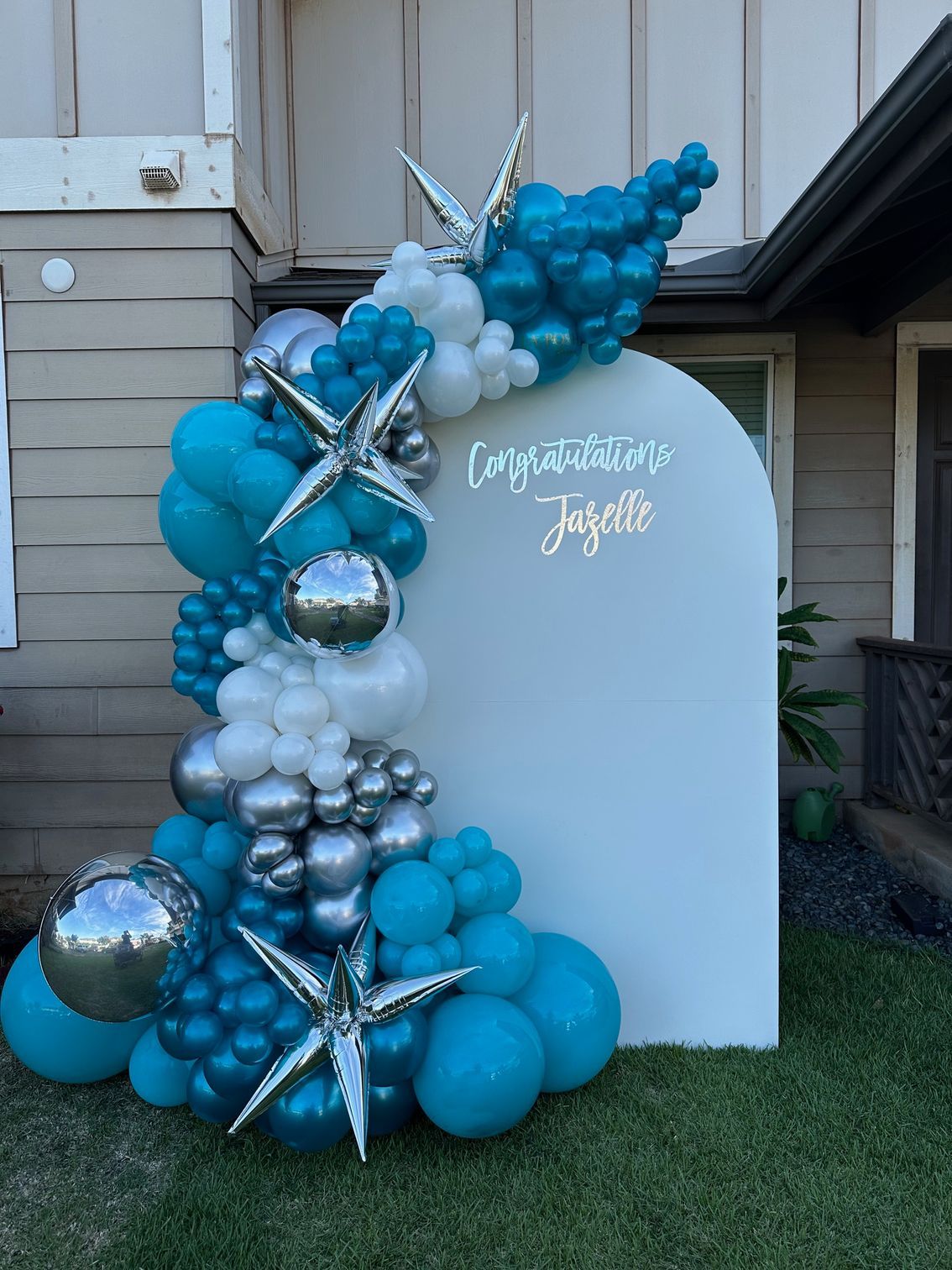 A bunch of blue and white balloons are sitting in front of a house.