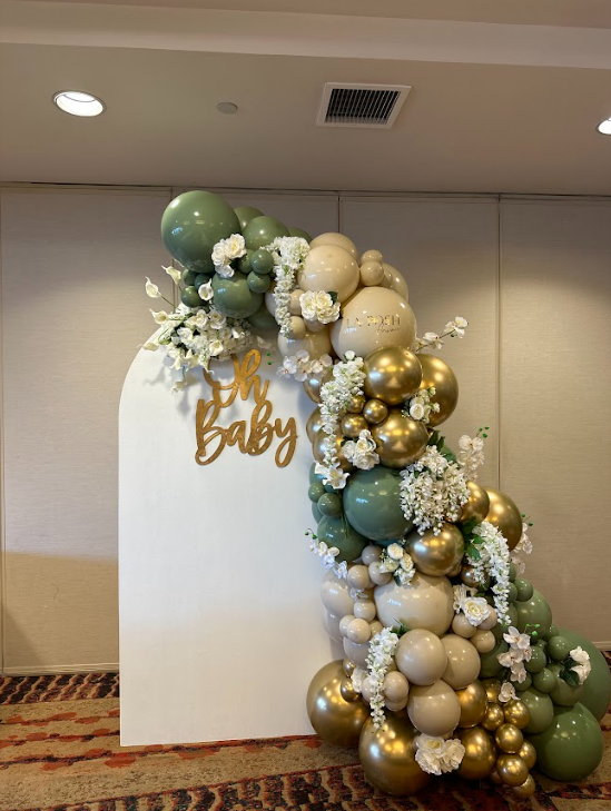 A wall decorated with balloons and flowers for a baby shower.
