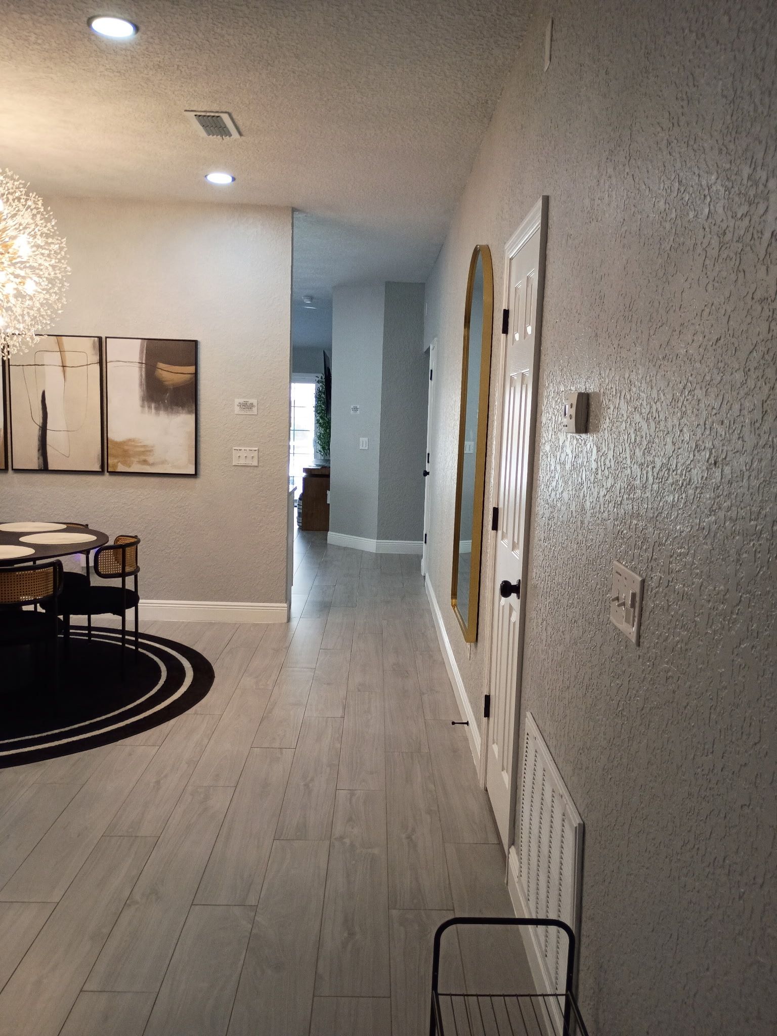 Hallway with textured silver walls, white door, and light wood flooring leading to a living space.