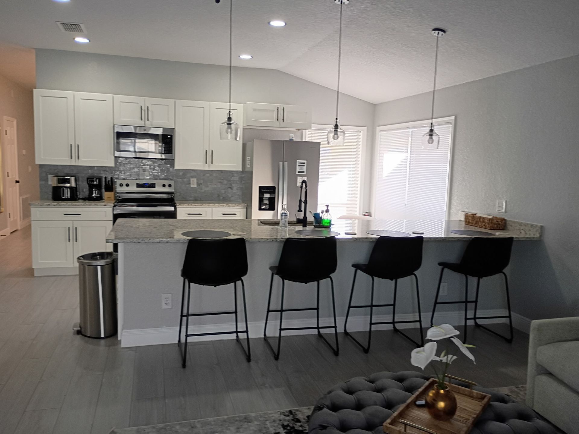 Modern kitchen with white cabinets, stainless steel appliances, and a breakfast bar with black stools.