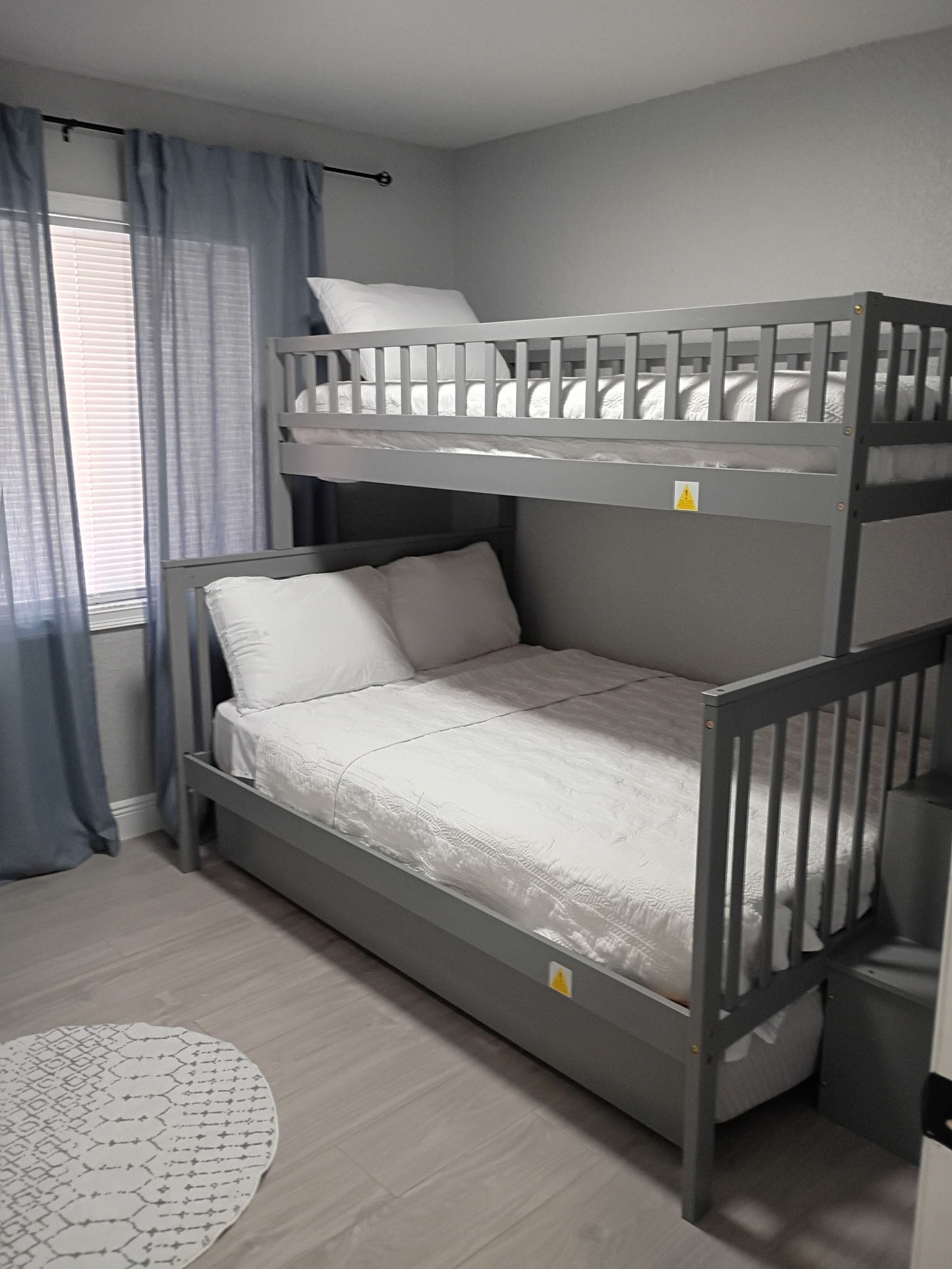 Gray bunk bed in a bedroom with white bedding and light blue curtains.