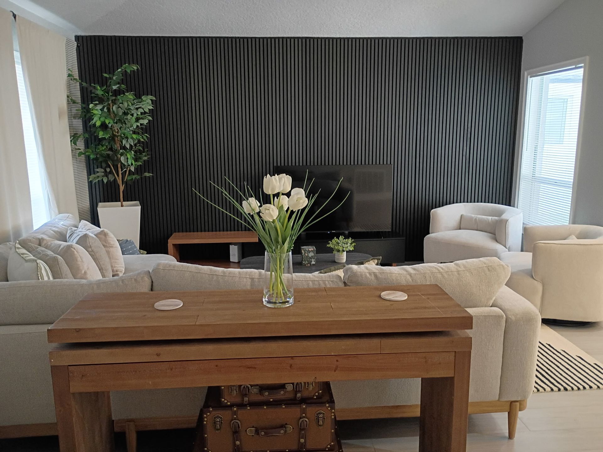 Living room with a wooden table and a vase of white flowers in front of a gray textured accent wall.