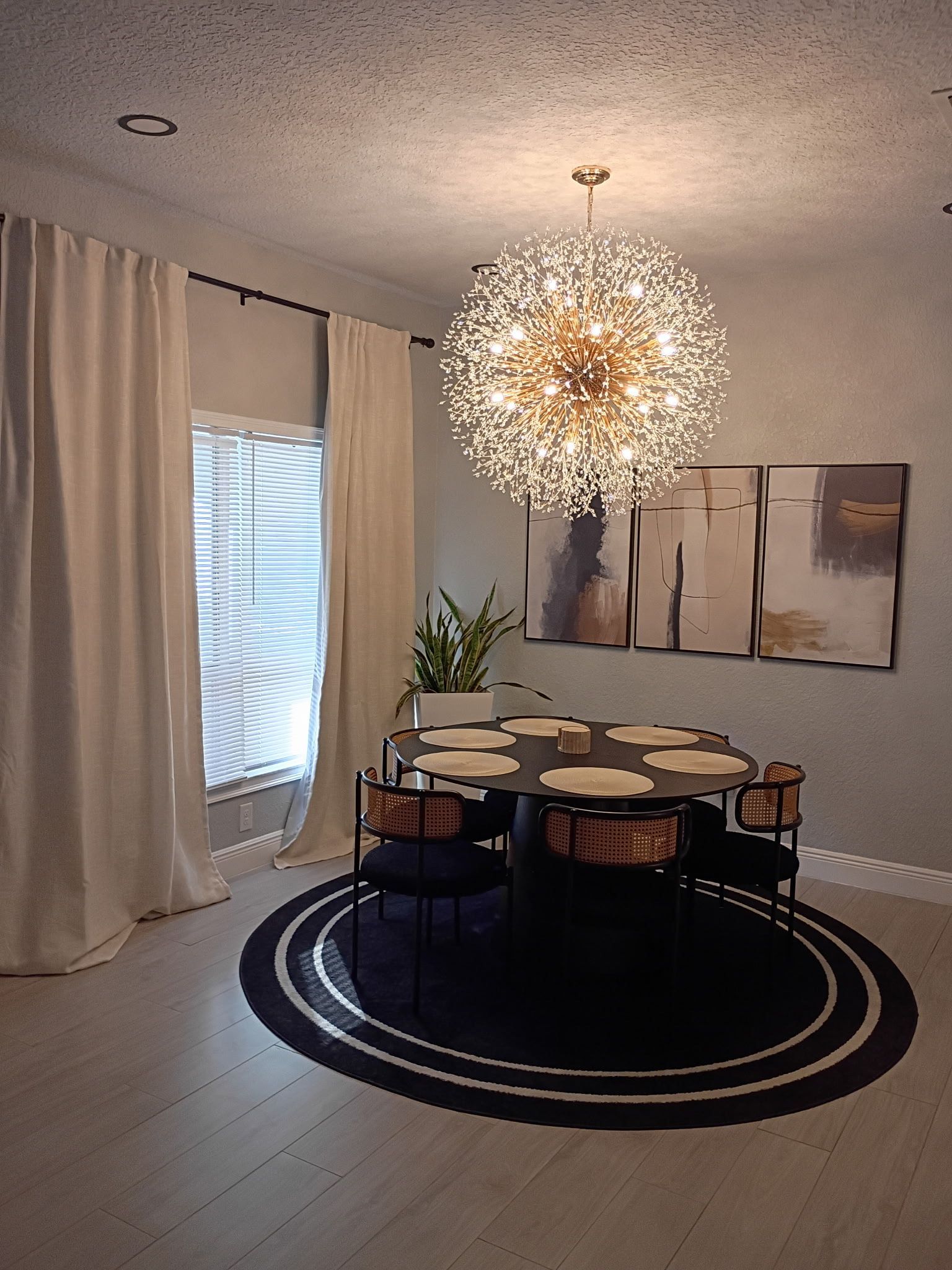 Dining room with chandelier, table, chairs, art, curtains, and round rug.