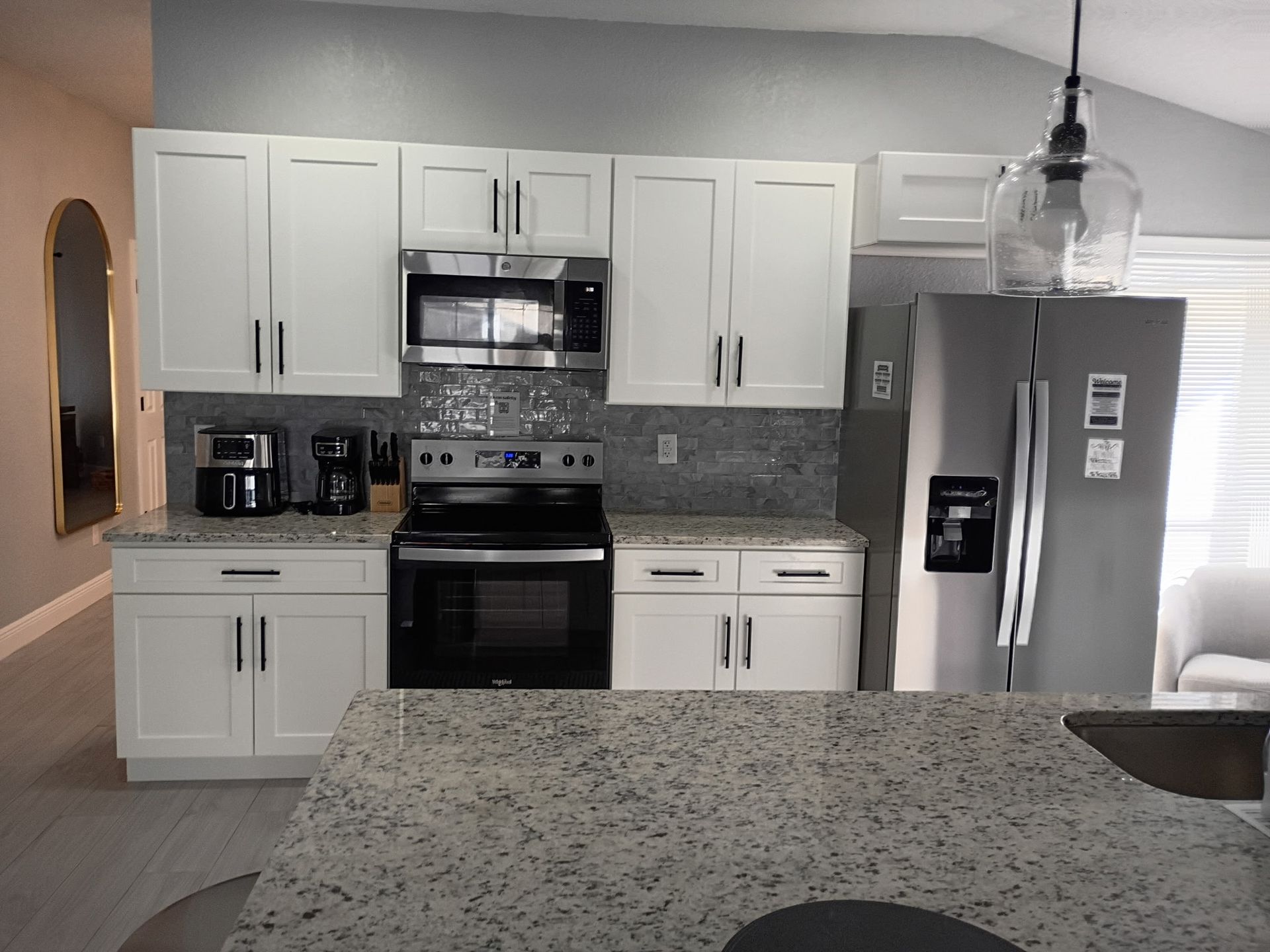 Modern kitchen with white cabinets, stainless steel appliances, and a granite countertop island.