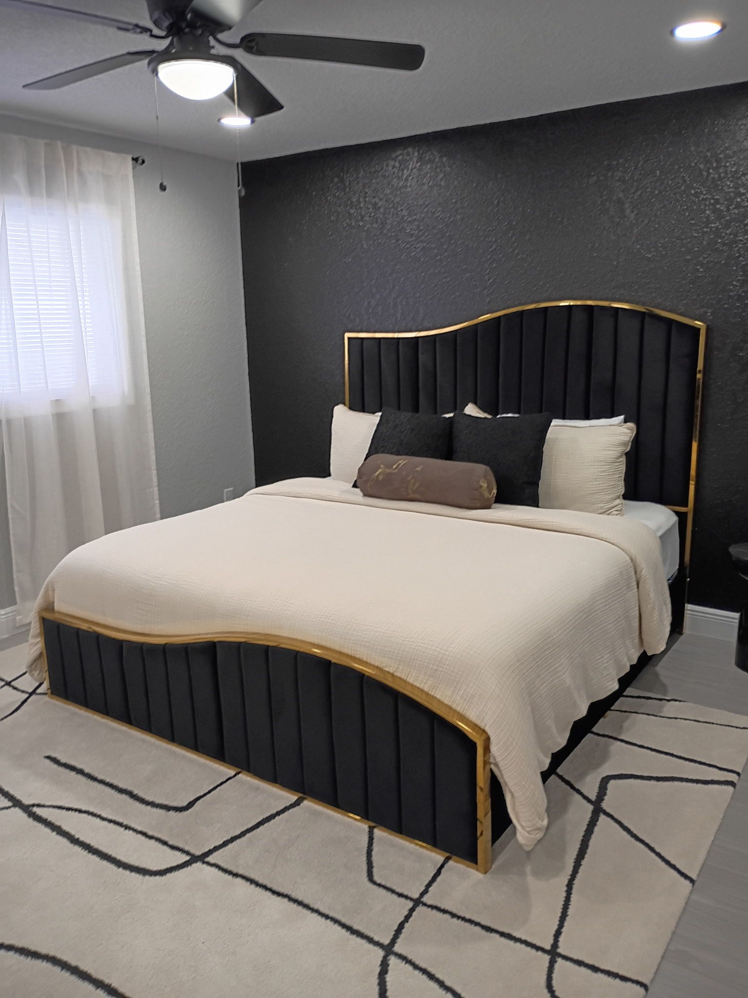 Bedroom with black bed frame, gold trim, black accent wall, and patterned rug.