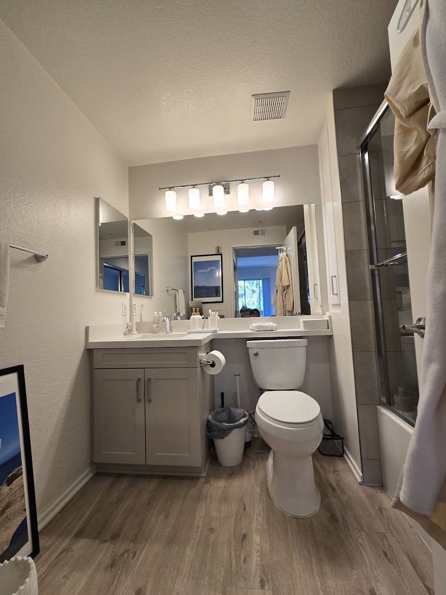 Bathroom with gray vanity, toilet, and shower. Gray and white color scheme, wood-look flooring.