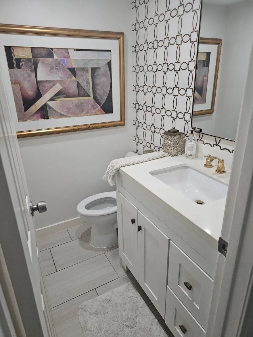 Bathroom with white vanity, toilet, and artwork; framed abstract art, patterned shower curtain.