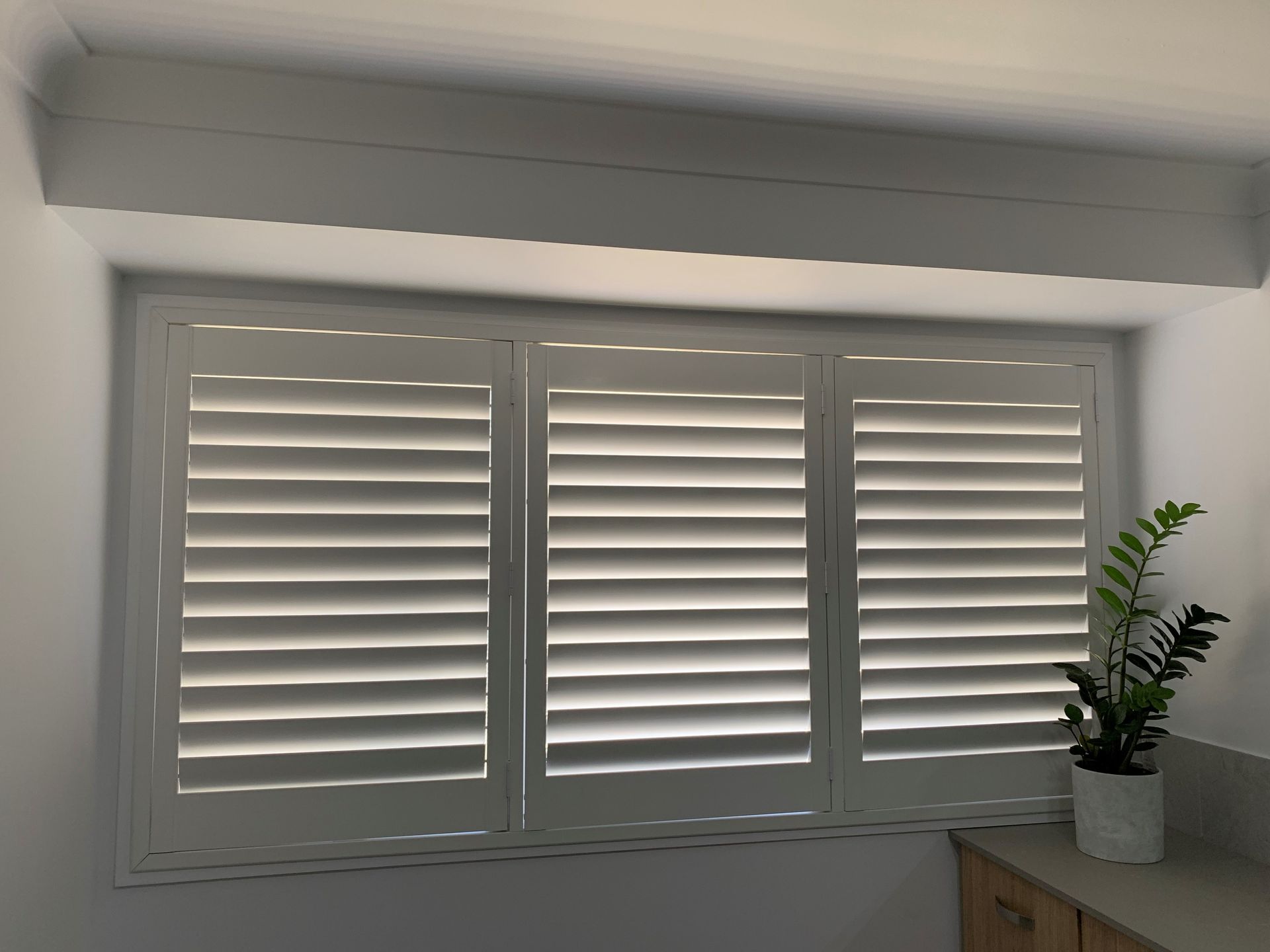 A bedroom with a bed , dresser , and shutters on the windows.