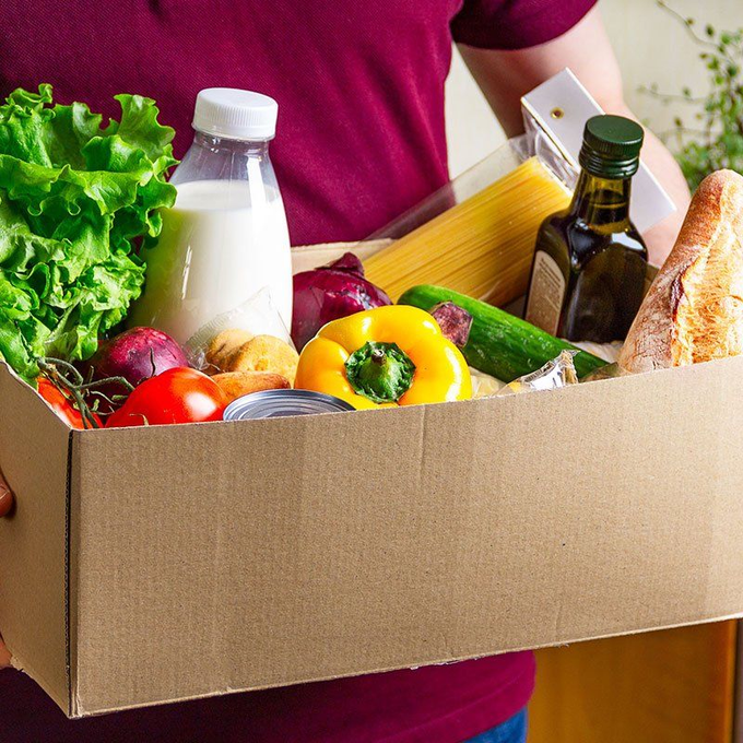 A person is holding a cardboard box filled with fruits and vegetables.