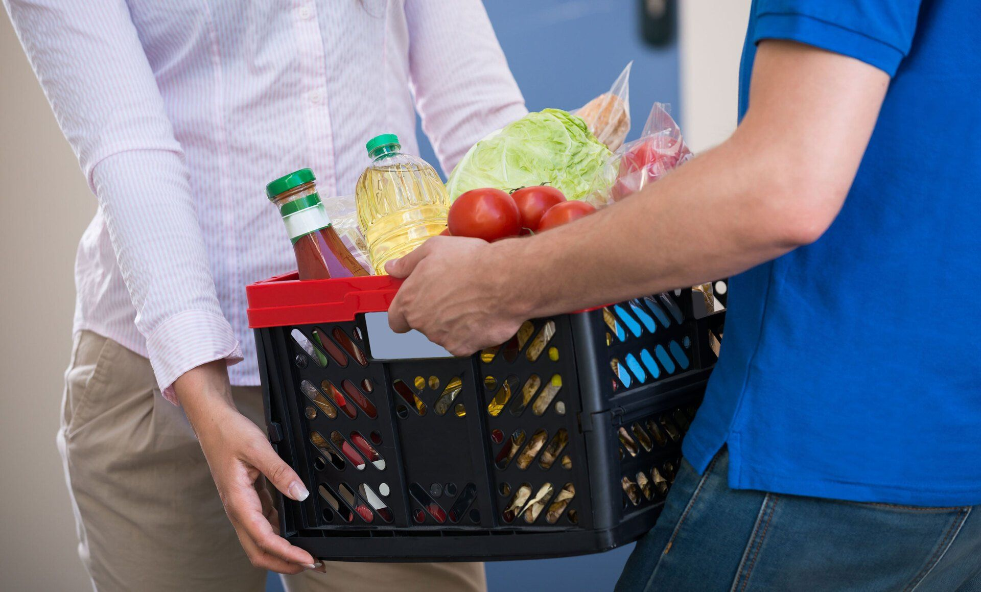 A man is carrying a basket of groceries to a woman.