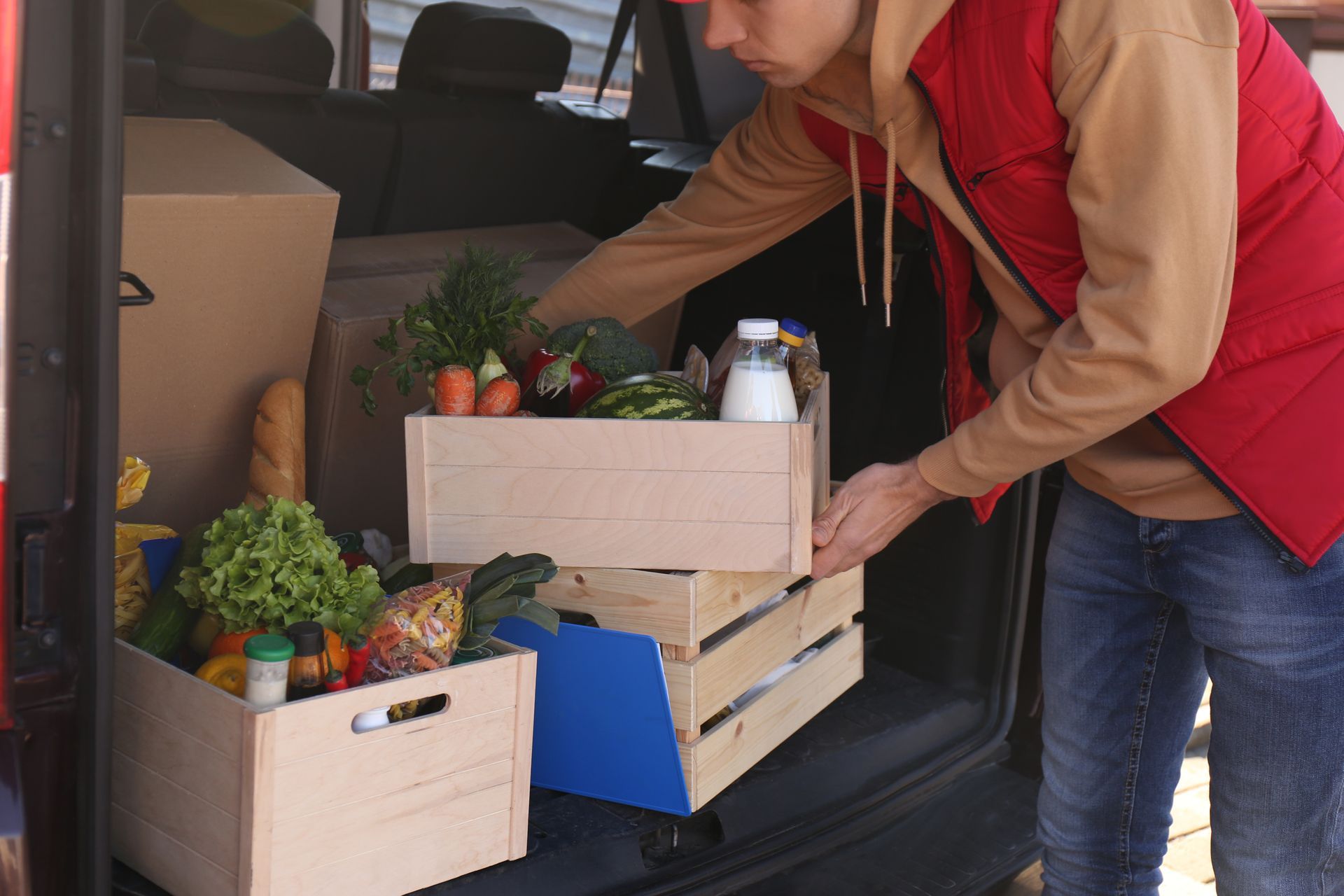 A man is putting wooden crates of food in the back of a van.