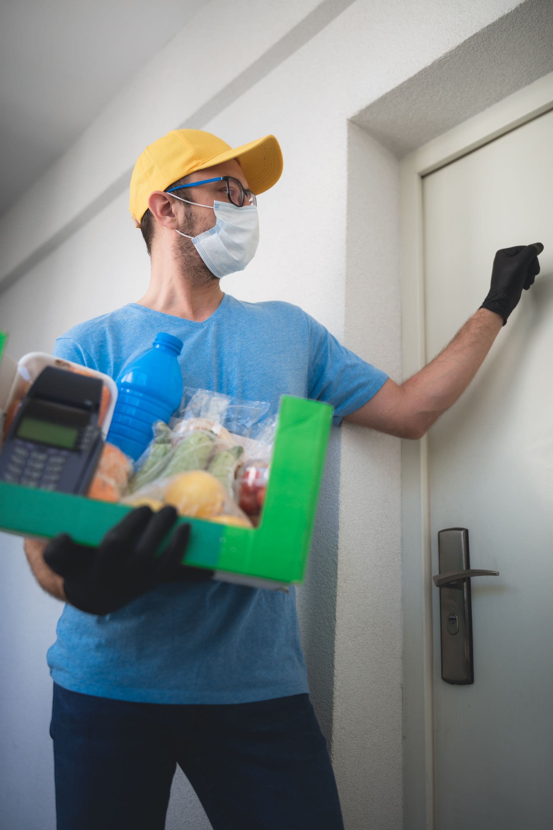 A delivery man wearing a mask and gloves is holding a box of food.