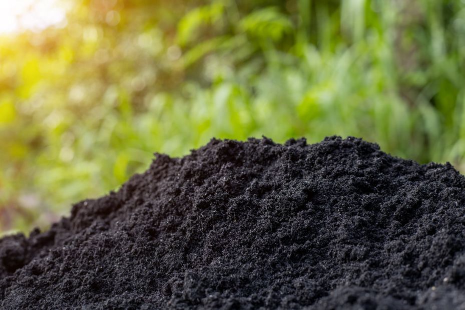 A pile of black soil is sitting in front of a green field.