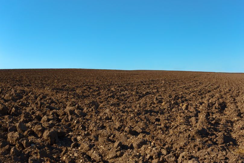 A field of brown dirt with a blue sky in the background