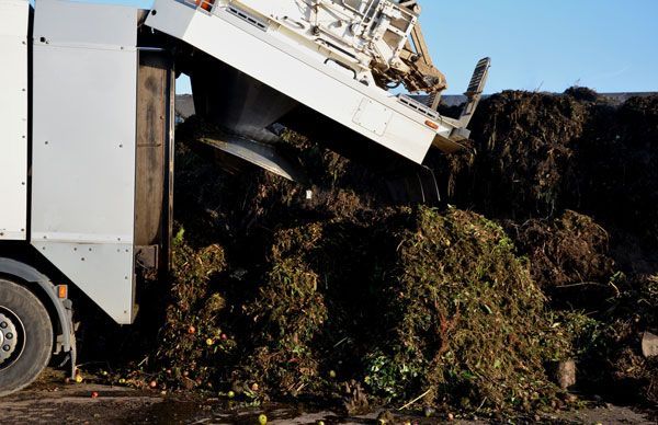 A garbage truck is dumping a pile of leaves into a pile.