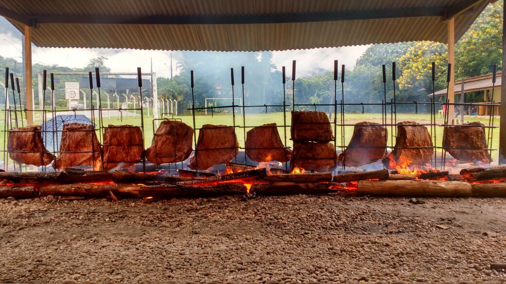 Um monte de carne está cozinhando em uma grelha sob um telhado.