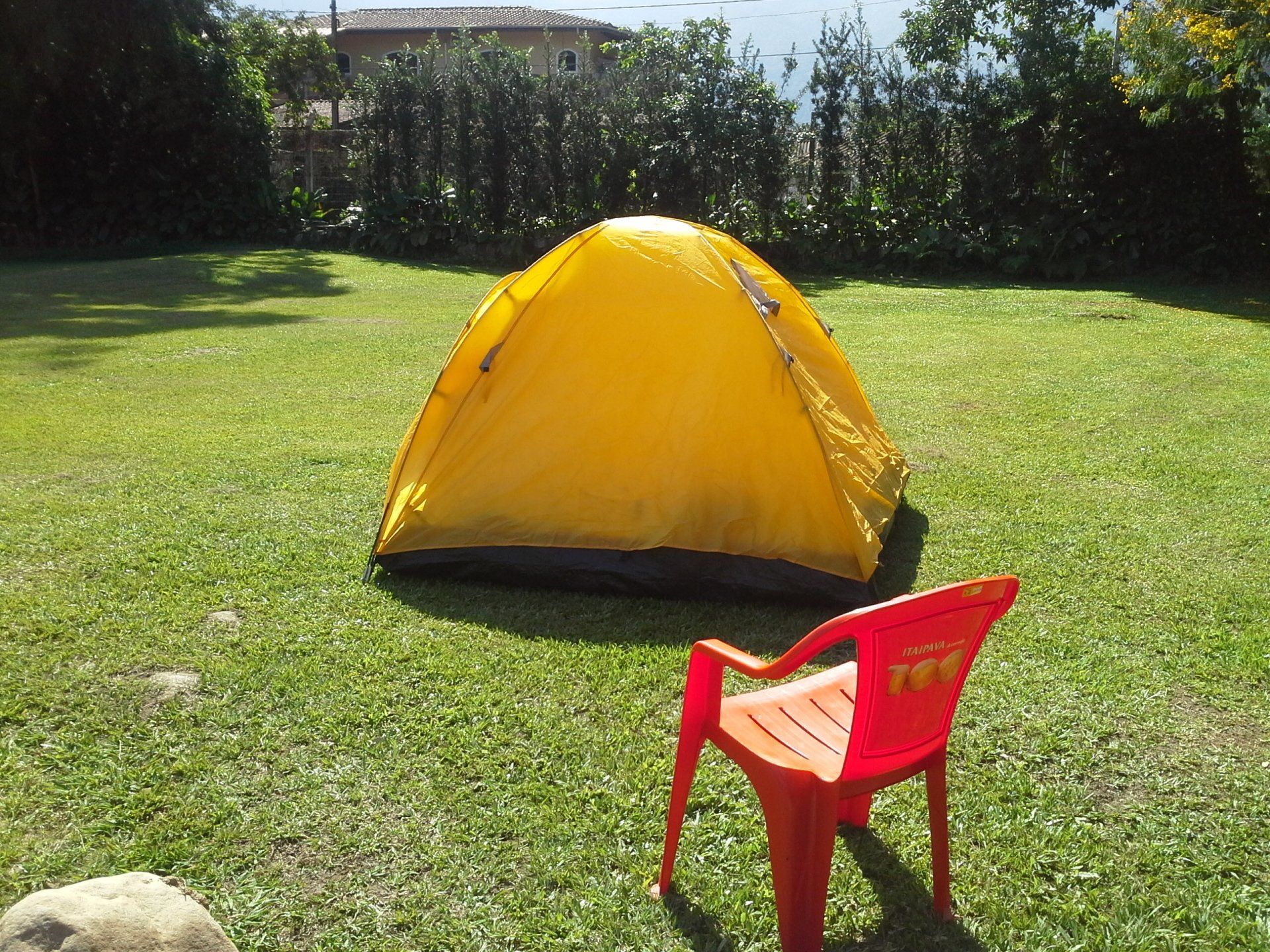 Uma tenda amarela está sentada na grama ao lado de uma cadeira vermelha