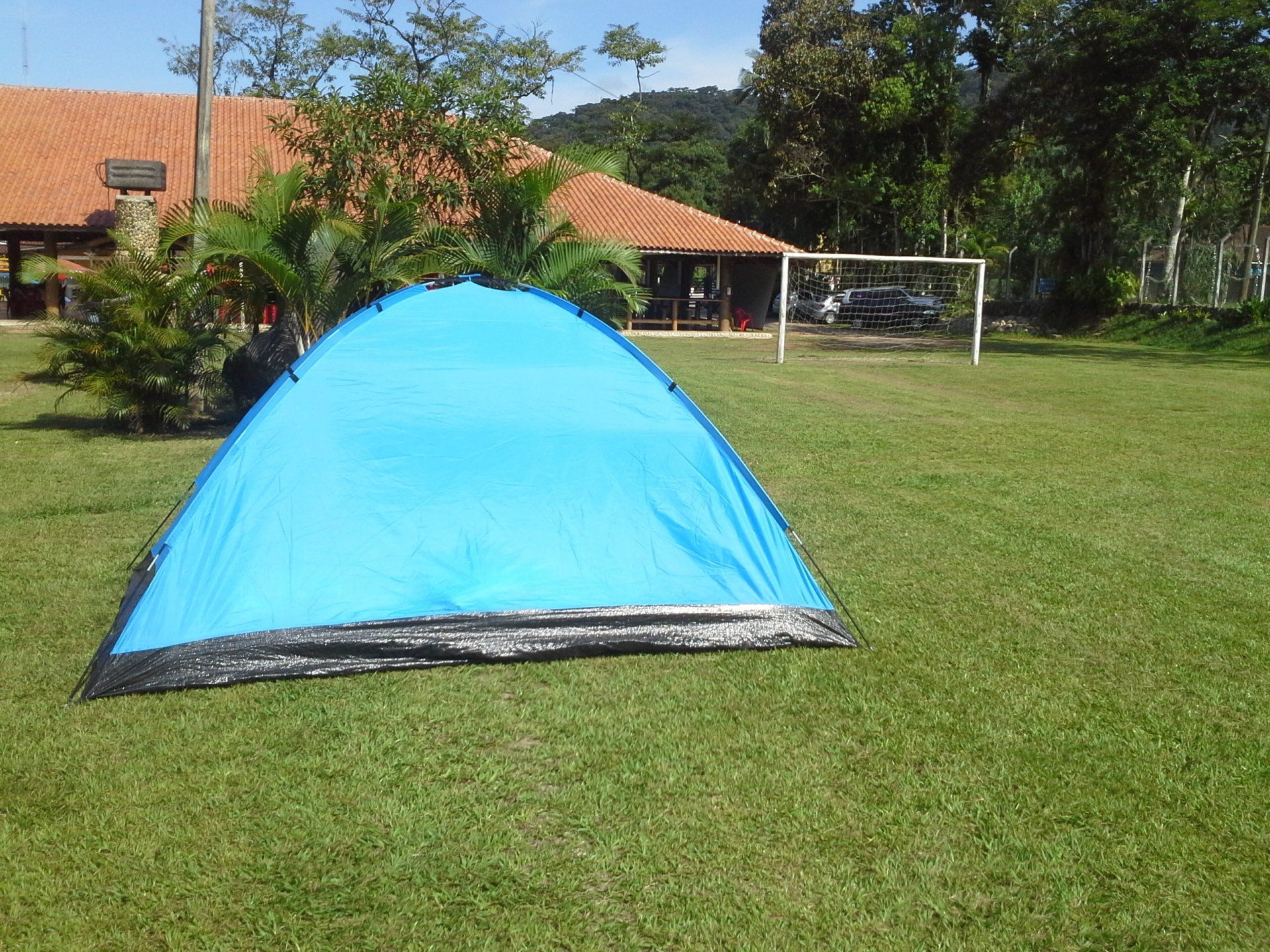 Uma tenda azul está na grama em frente a um gol de futebol.