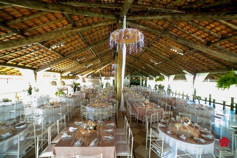 Uma grande sala cheia de mesas e cadeiras sob um telhado de madeira.