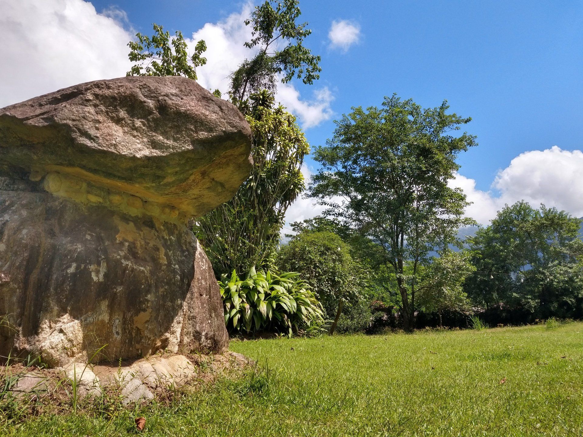 Uma grande pedra está no meio de um campo gramado.