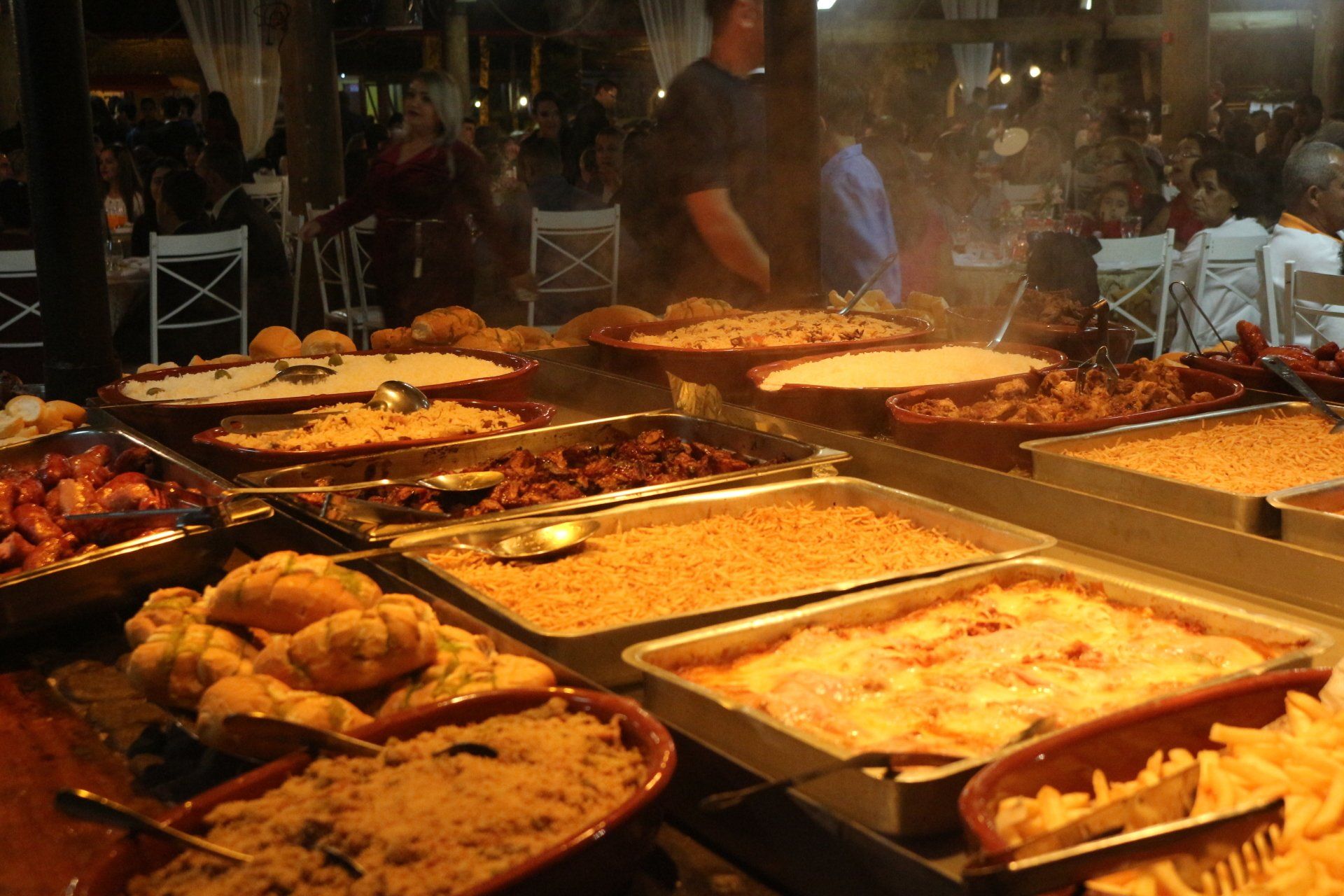 Uma mesa de bufê cheia de comida e um homem parado atrás dela.