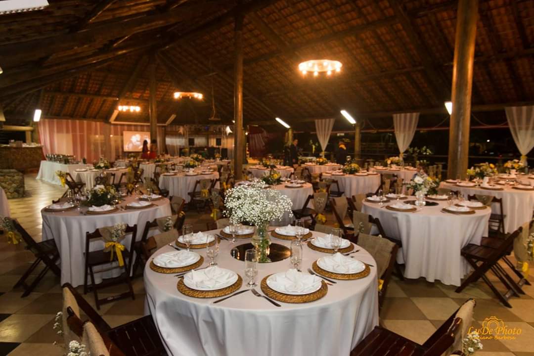 Uma grande sala com mesas e cadeiras preparadas para uma recepção de casamento.