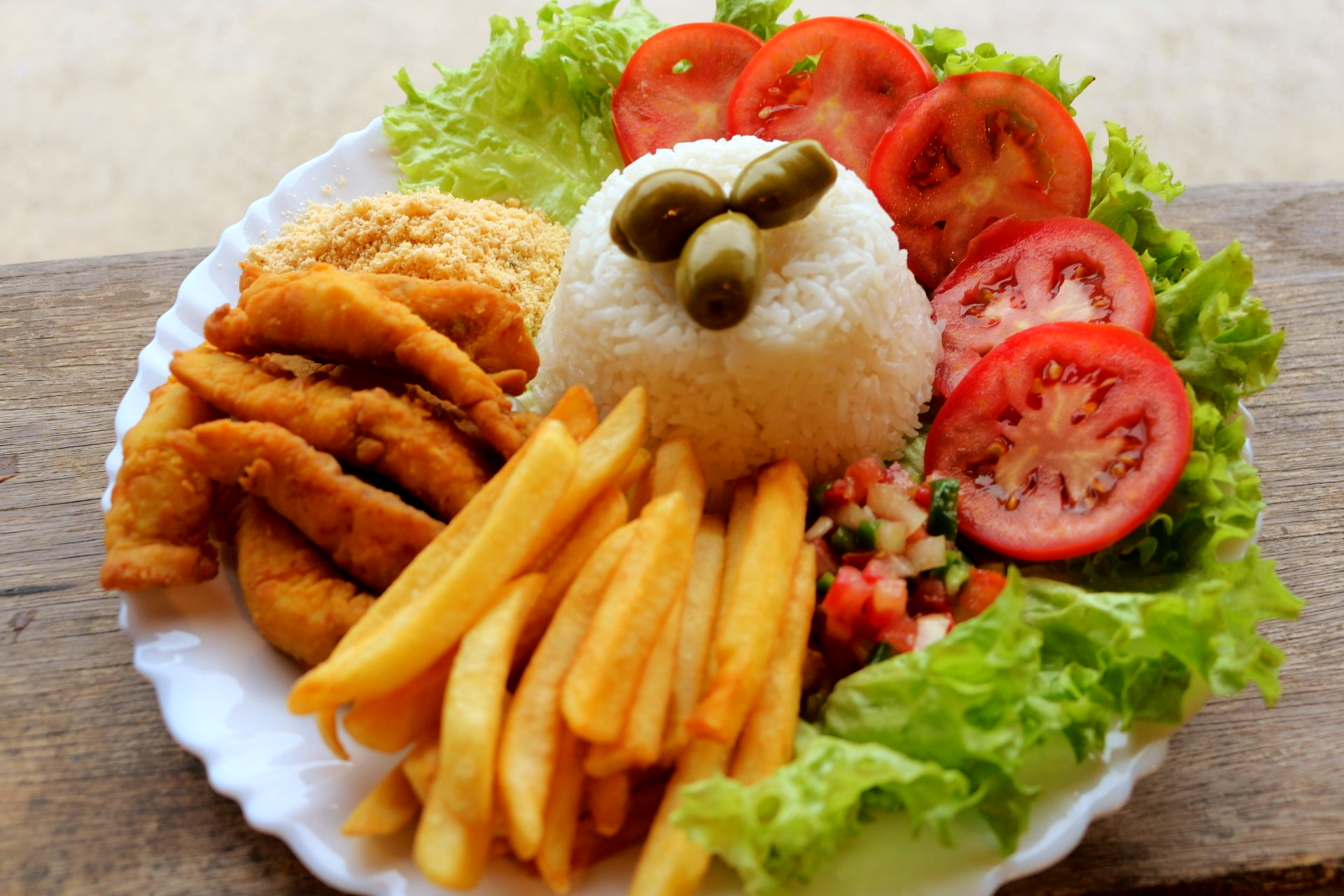 Um prato de comida com batatas fritas, arroz, tomate e alface em uma mesa de madeira.
