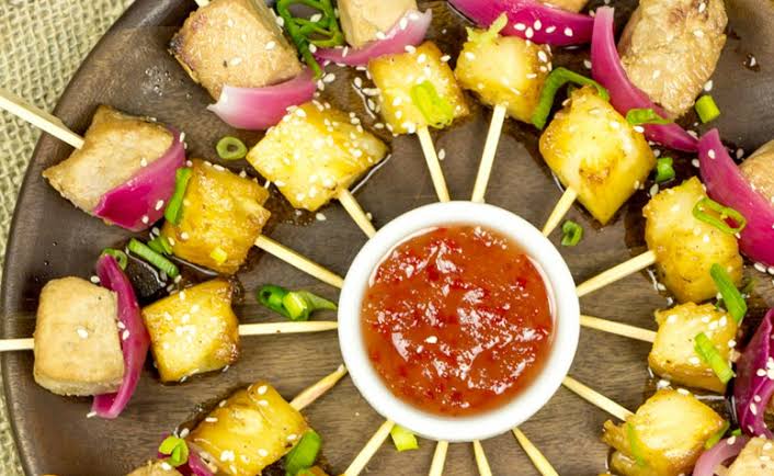 Um prato de comida com espetos e uma tigela de molho sobre uma mesa.
