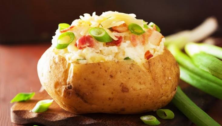 Uma batata assada recheada com arroz e cebolinha em uma tábua de madeira.