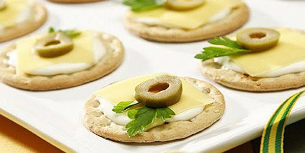 Um prato branco coberto com biscoitos com queijo e azeitonas.