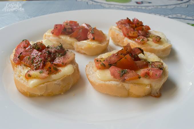 Um prato branco coberto com quatro pedaços de comida com tomate e queijo.