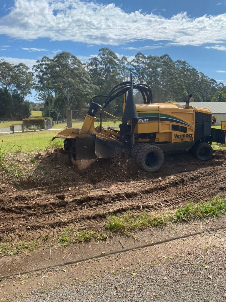 A Yellow Stump Grinder Grinding Wood Into Mulch in a Grassy Area — MNC Trees in Wauchope, NSW
