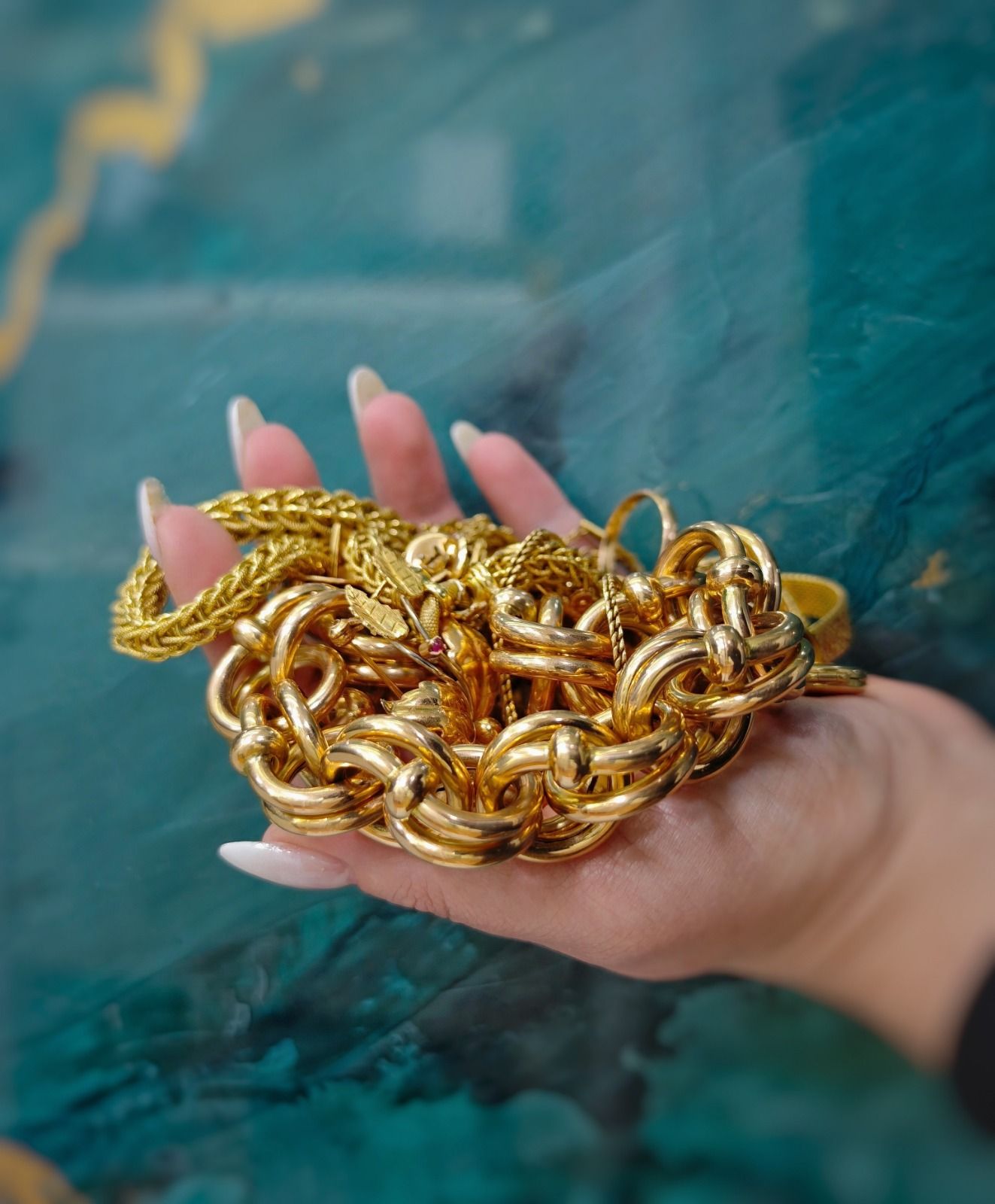 Mano che regge un braccialetto a catena d'oro aggrovigliato su una superficie blu