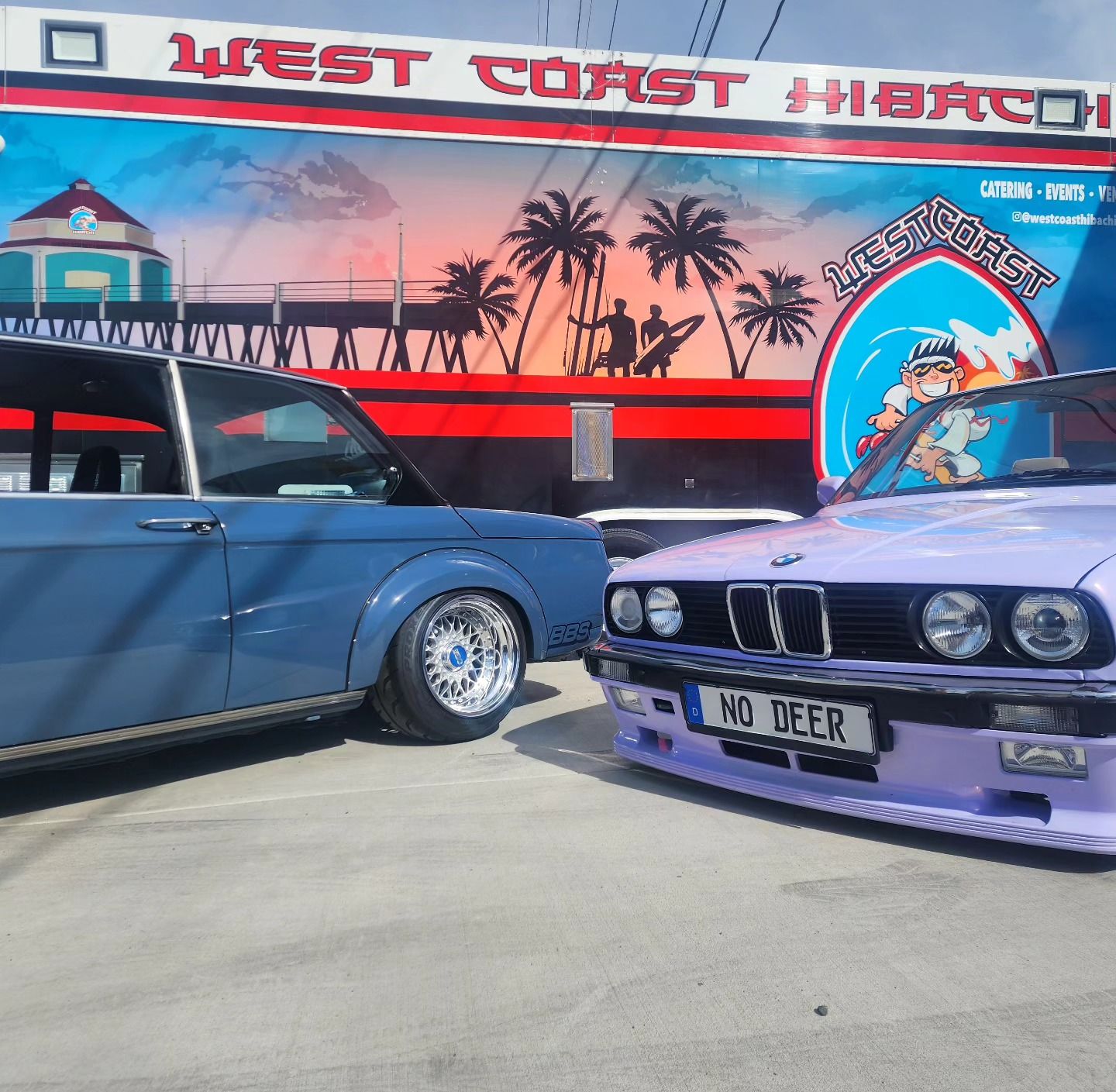 Two cars are parked in front of a sign that says west coast hibiscus