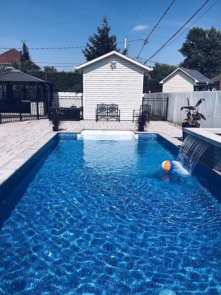 Une grande piscine avec une cascade et un cabanon en arrière-plan.