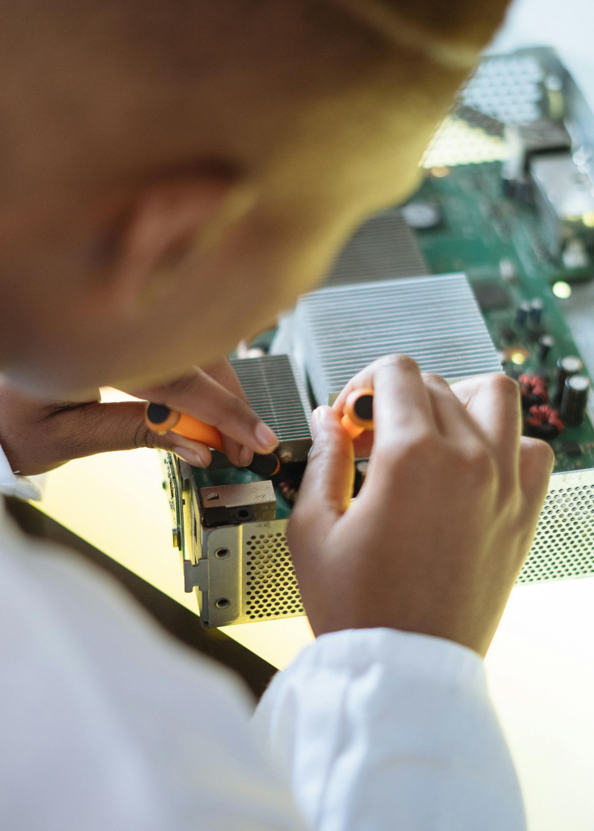 Person in white lab coat using tools on circuit board.