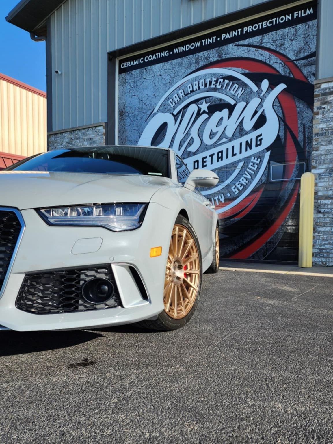 A light gray Audi parked in front of Olson's Detailing, a car care business.