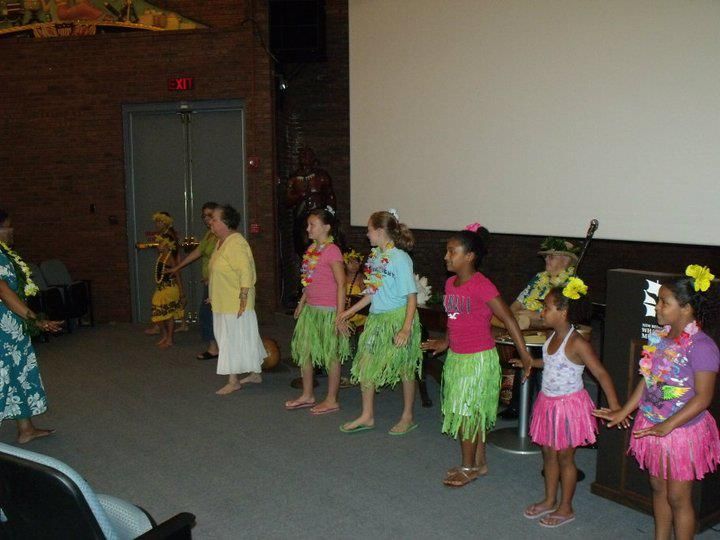 A group of girls in hawaiian skirts are dancing in a room