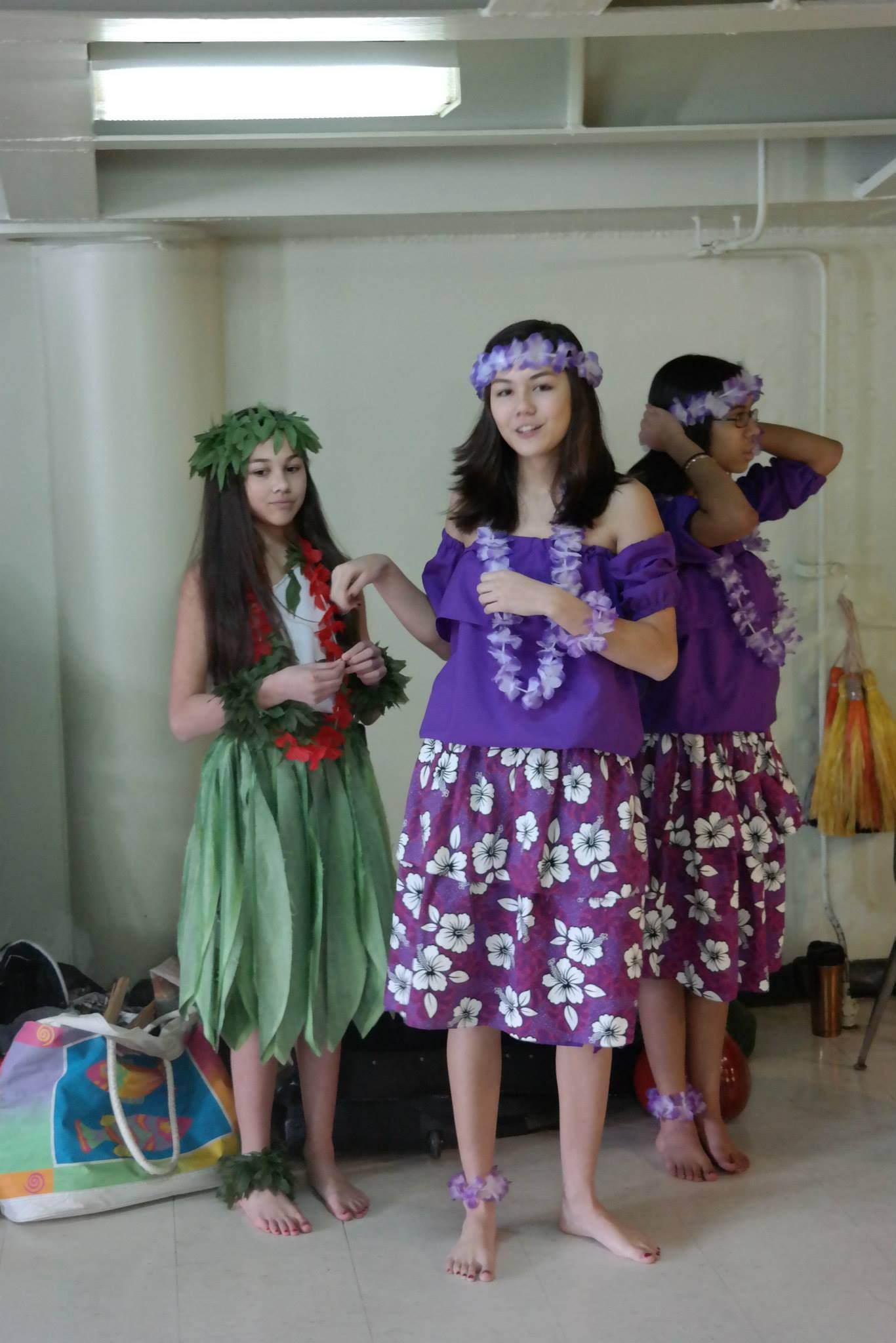 Three girls in hawaiian costumes are standing next to each other