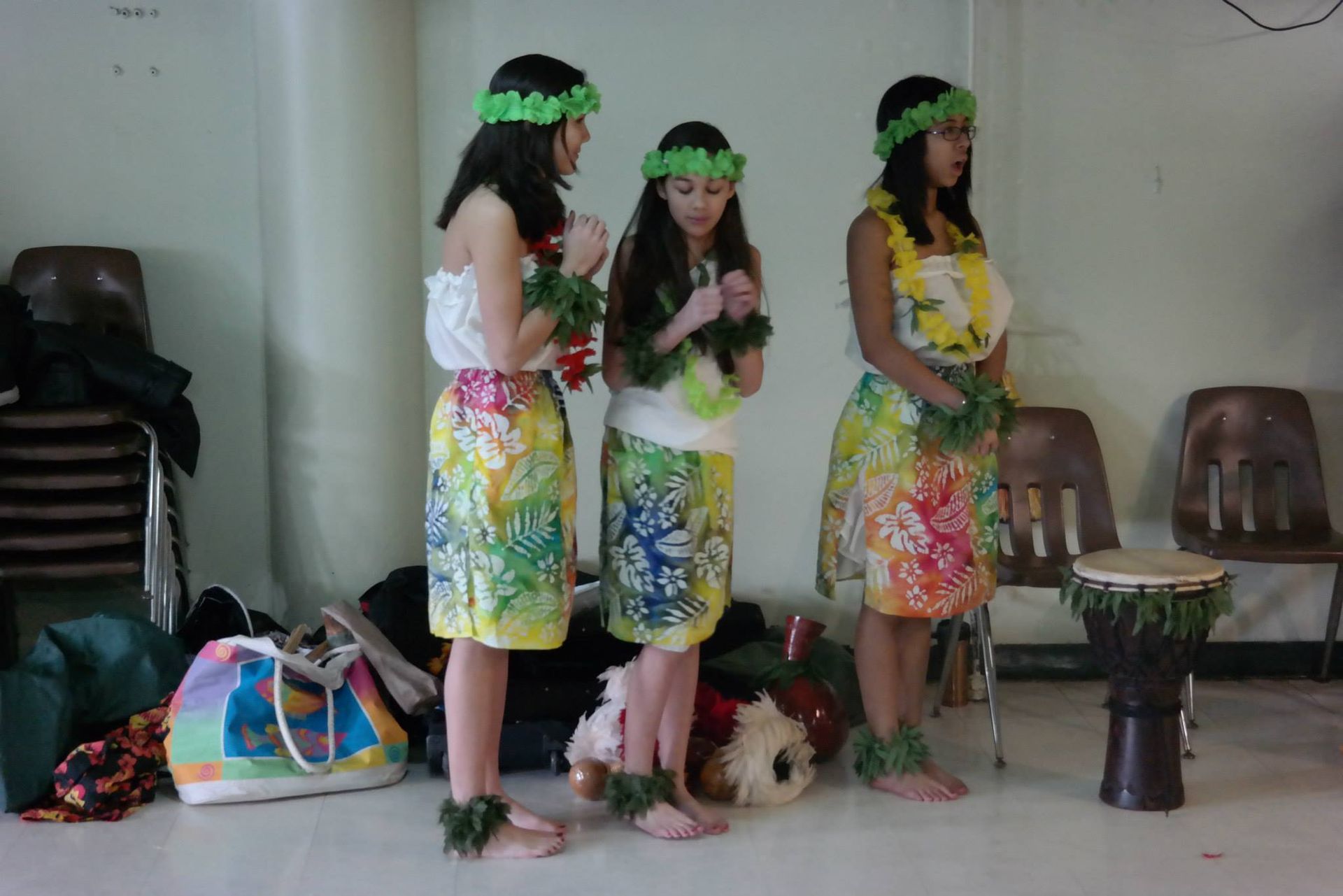Three girls in hawaiian costumes are standing next to each other