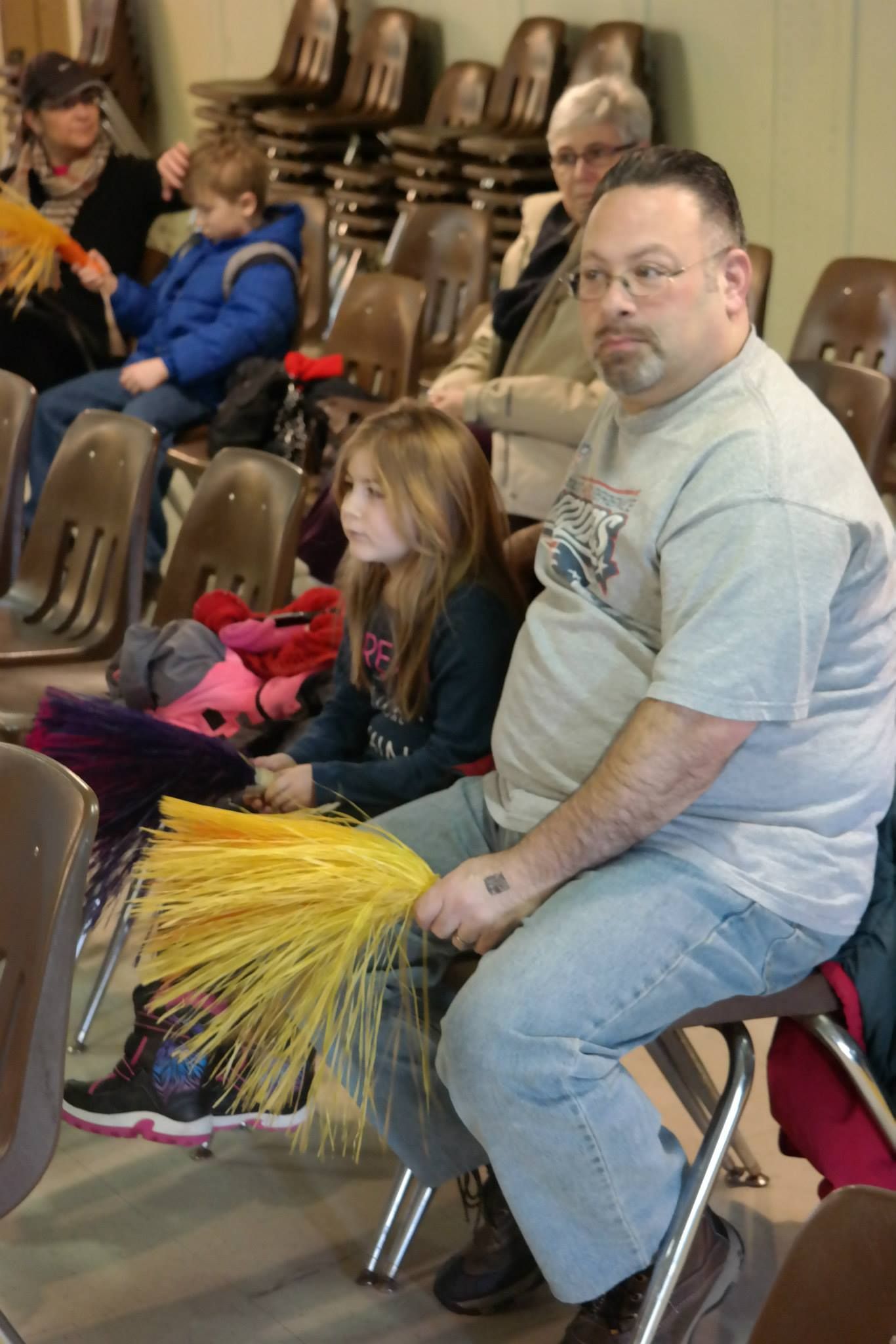 A man and a girl are sitting in chairs holding pom poms.
