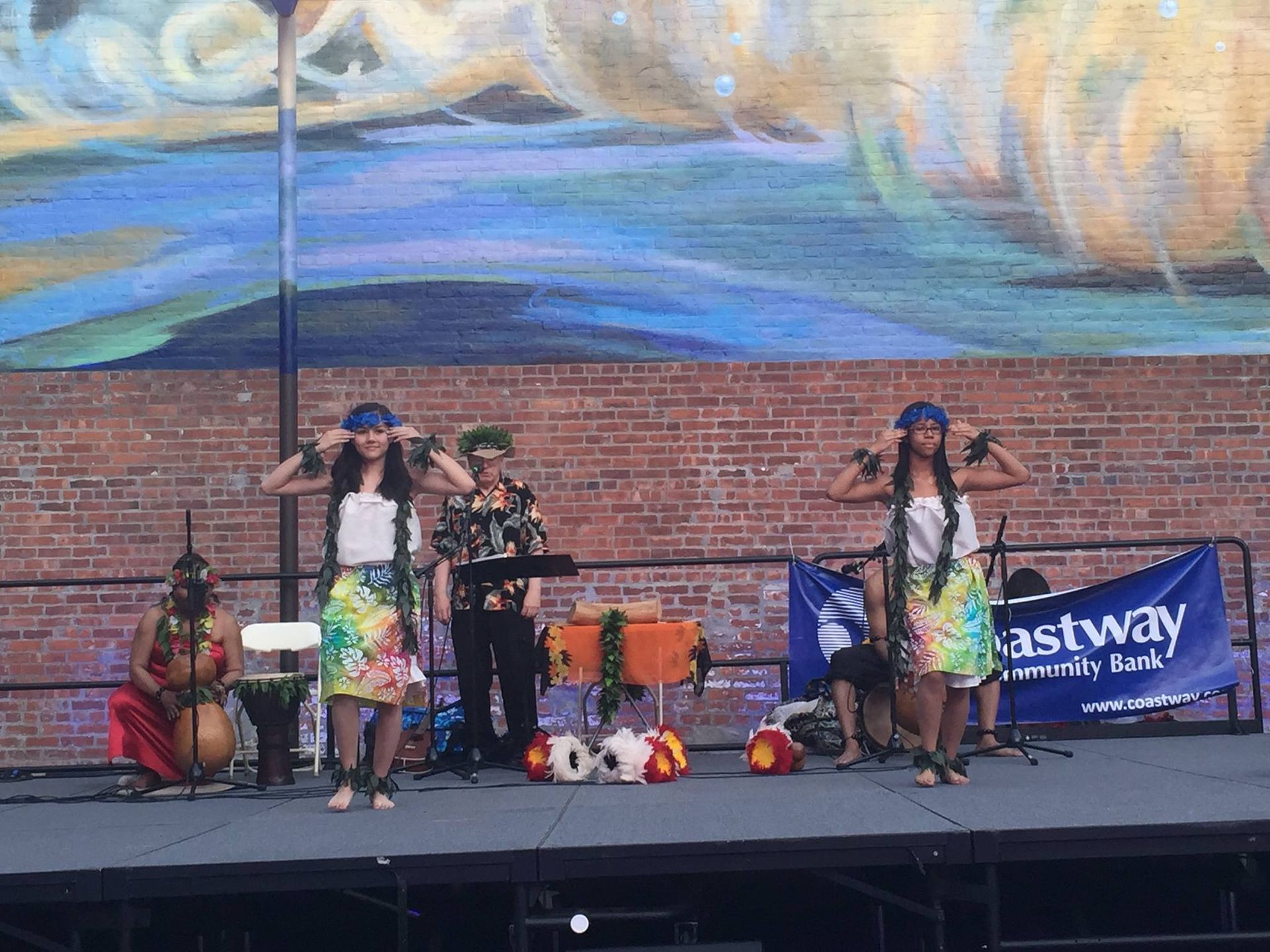 A group of people are standing on a stage in front of a mural.