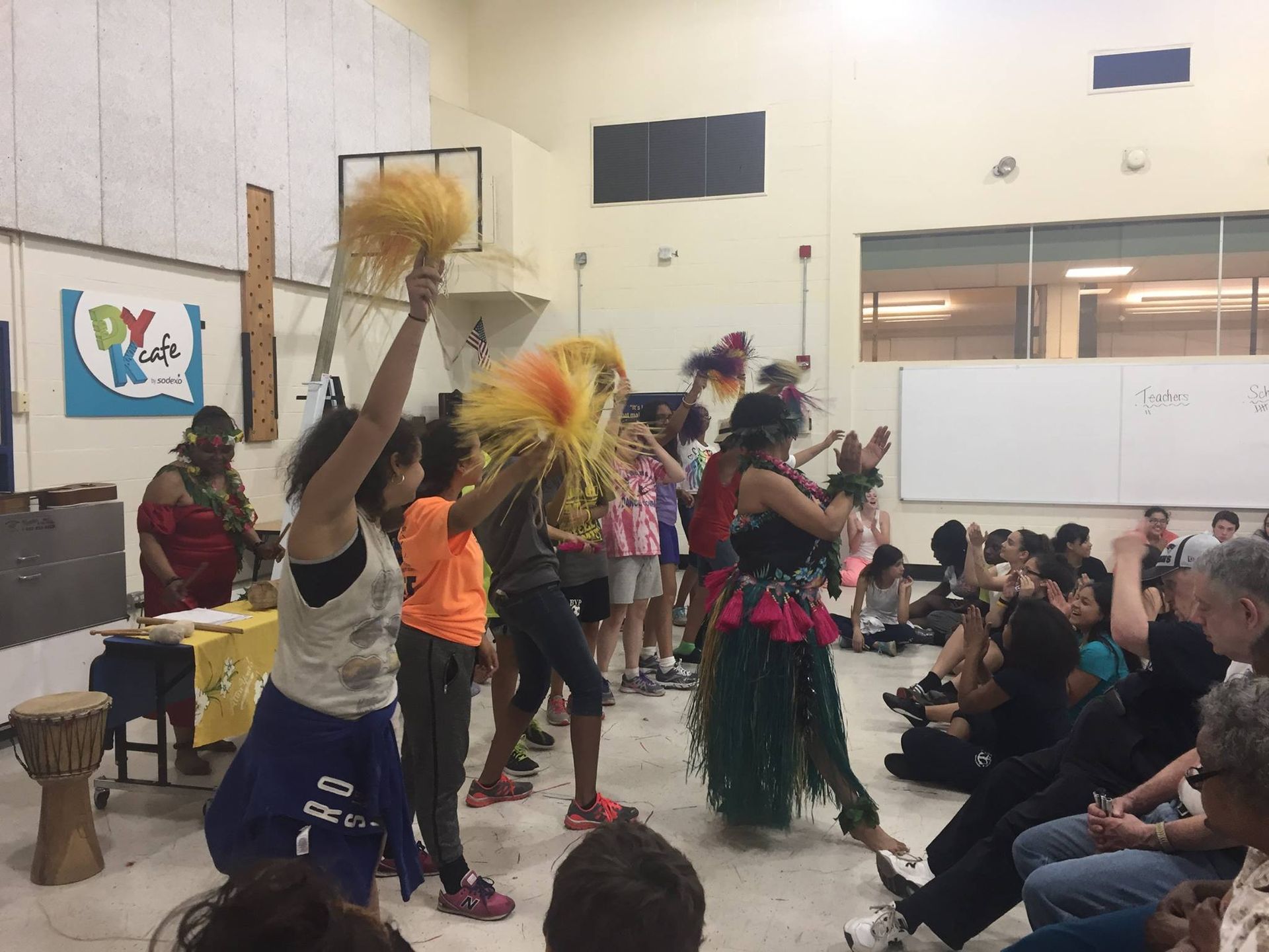 A group of people are dancing in a room with a basketball hoop in the background.