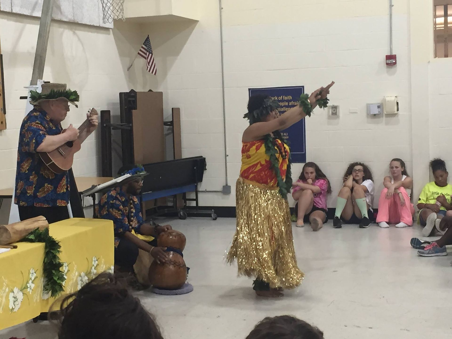 A woman is dancing in front of a group of children while a man plays an ukulele.