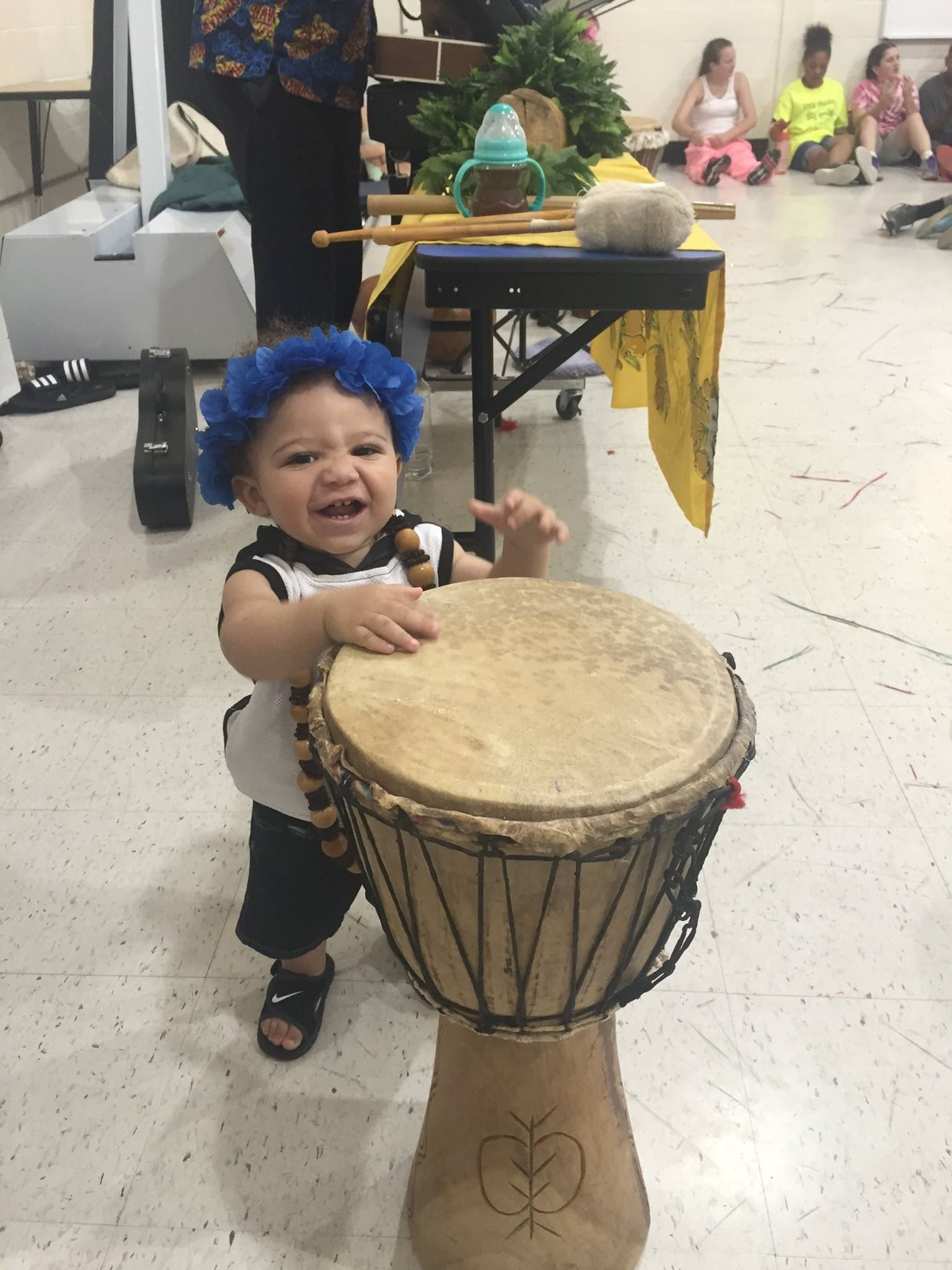 A baby in a blue hat is playing a drum