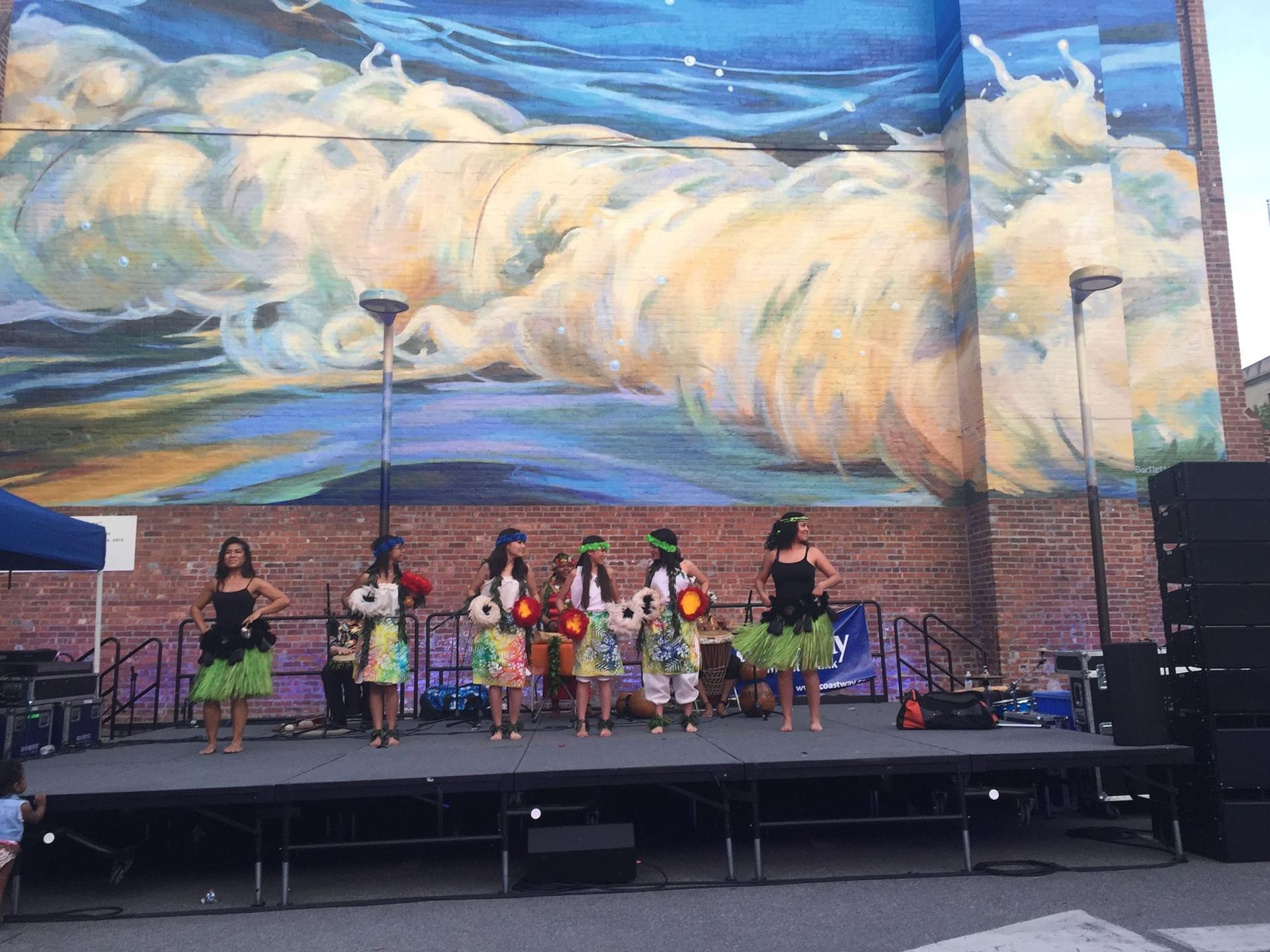 A group of people are dancing on a stage in front of a large mural.