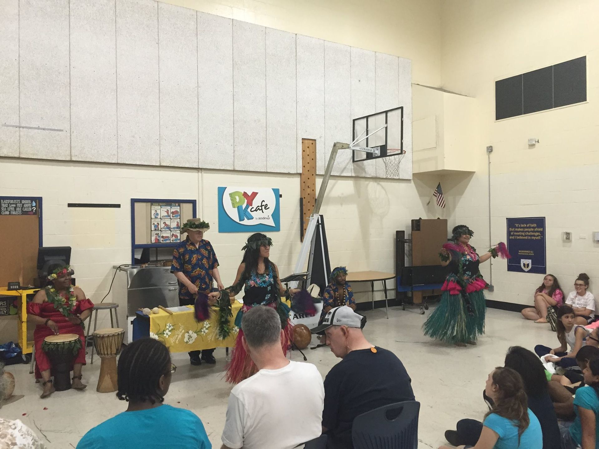 A group of people are watching a hula performance in a gym.